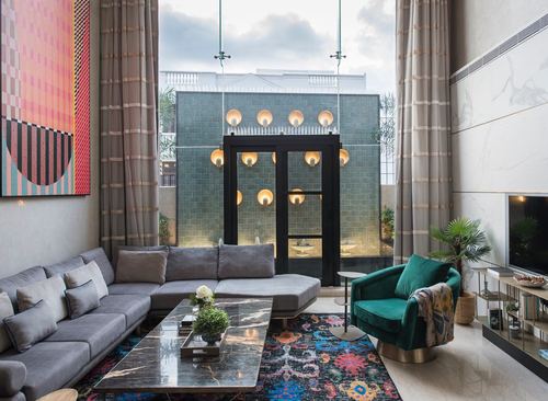 Double-height living room with grey sectional, marble table, and glass doors to a tiled courtyard with pendant lights