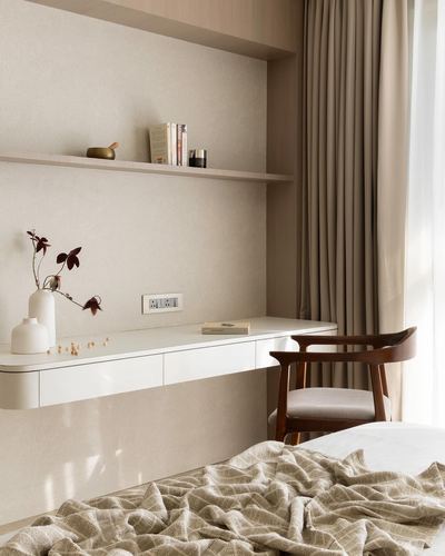 Beige bedroom corner with floating desk, wooden armchair, and curtained window
