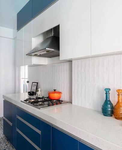 Modular kitchen with navy blue cabinets, white countertop, steel hood, and orange pot on stove