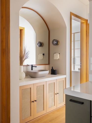 Arched bathroom niche with wood-framed mirror, vessel sink, and cane cabinetry