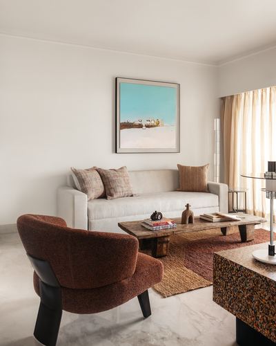 Living room with beige sofa, rust bouclé chair, wood coffee table and framed art