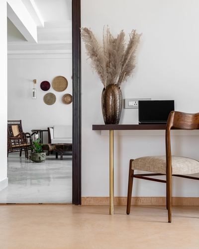 Console desk with pampas grass vase and wooden chair beside doorway to living room