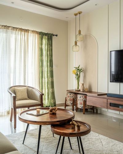 Living room with round nested wood tables, cane armchair, green floral curtain, and arched niche with pendant lights
