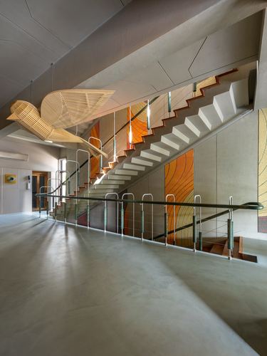 Staircase with glass railing beneath a suspended wooden bird sculpture and orange mosaic wall art