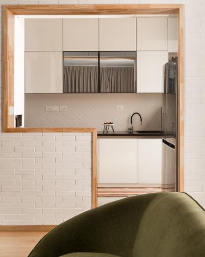 Kitchen seen through a wooden-framed brick wall opening, green armchair in foreground