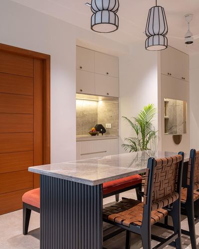 Dining area with fluted table base, woven leather chairs, and drum pendant lights beside a wooden door