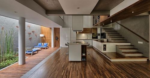 Open-plan interior with wood floors, white kitchen island, and floating wooden staircase