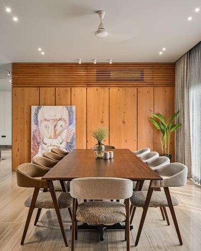 Dining room with long wooden table, mixed upholstered chairs, and a fluted wood-panelled wall with framed art.