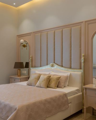 Blush pink bedroom with tufted fabric headboard wall, gilt bed frame, and arched mirror sconce