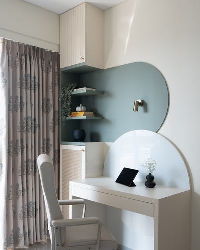 Study nook with curved sage wall panel, built-in shelving, cane chair, and desk near patterned curtain