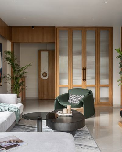 Living room with green curved armchair, dark nesting tables, and fluted-glass wood wardrobe wall.