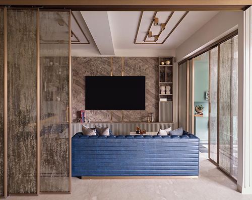 Living room with blue channel-tufted sofa against a marble feature wall and brass ceiling detailing