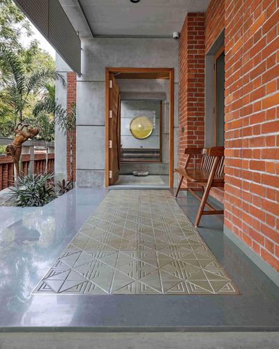 Covered brick and concrete passage with patterned stone floor runner leading to open wooden door