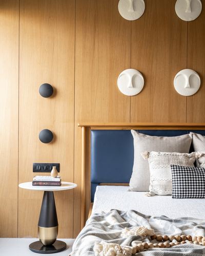 Wood-panelled bedroom corner with navy leather headboard, round marble side table, and sculptural wall discs