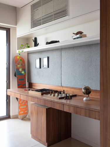 Wood study desk with chess set and globe beneath a grey fabric-paneled wall and floating shelf