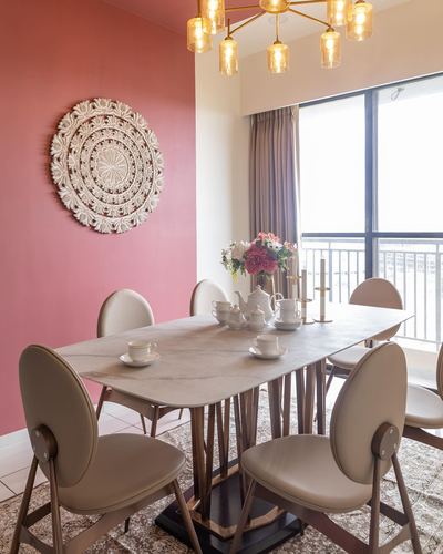 Dining table set with tea service under brass chandelier against pink wall with carved wood medallion