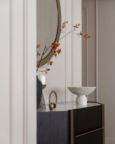 Foyer console with stone bowl, round mirror, and orange branch decor seen through doorway