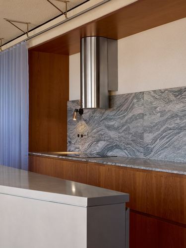 Kitchen corner with wood cabinetry, veined stone backsplash, and cylindrical steel range hood