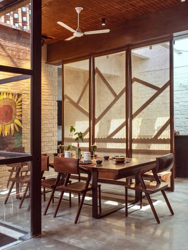 Wooden dining table with cane screen wall casting geometric shadows in brick interior