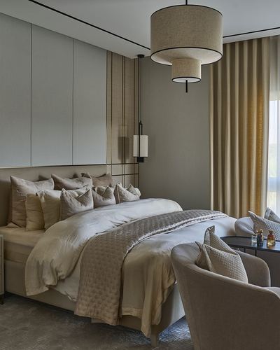 Neutral-toned bedroom with layered drum pendant, tufted headboard, and beige curtains beside window