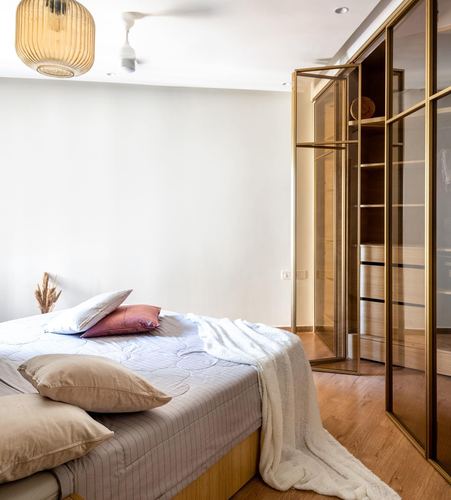 Bedroom with layered bedding and a brass-framed glass wardrobe beside wooden flooring