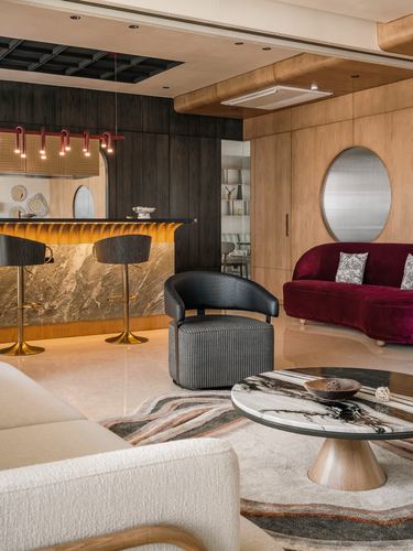 Living and bar area with dark wood paneling, marble bar counter, maroon velvet sofa and round marble coffee table