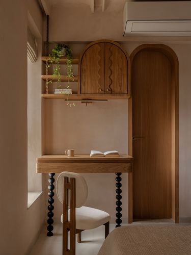 Wall-mounted wood desk with cabinet and shelving beside an arched wooden door in a warm-toned bedroom nook