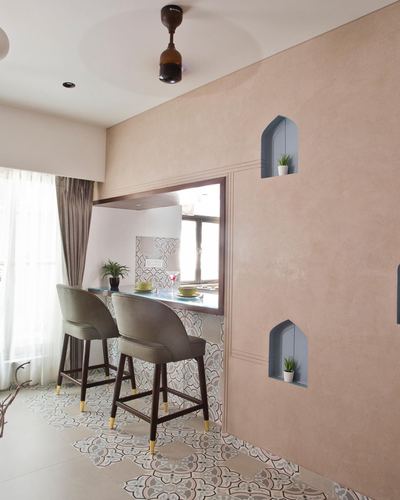 Blush plaster wall with arched niches beside a patterned-tile breakfast counter with two bar stools
