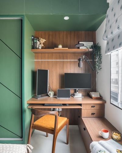 Compact home office nook with wood panelling, two monitors, and a mid-century wooden chair beneath a green ceiling.