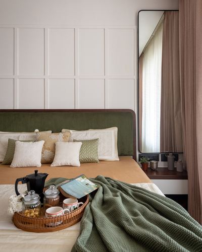 Bed with green upholstered headboard, tray of coffee and cushions, mirror reflecting curtained window