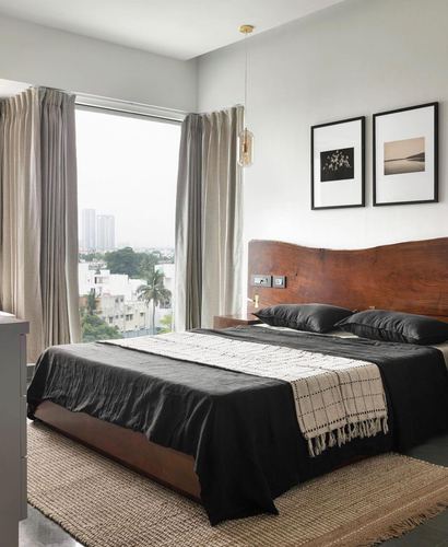 Bedroom with live-edge wood headboard, black linen bedding, jute rug and city view through window