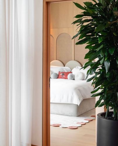 View through a doorway past a plant into a bedroom with an arched cane headboard wall