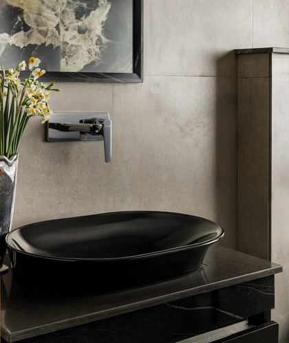 Black oval vessel sink on dark marble counter with chrome wall faucet against textured stone wall