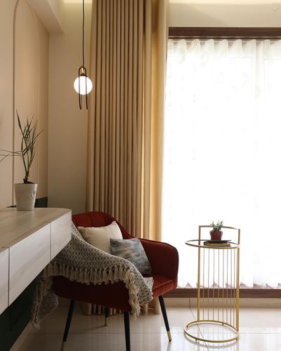 Terracotta velvet armchair beside gold side table under a globe pendant with sheer curtains