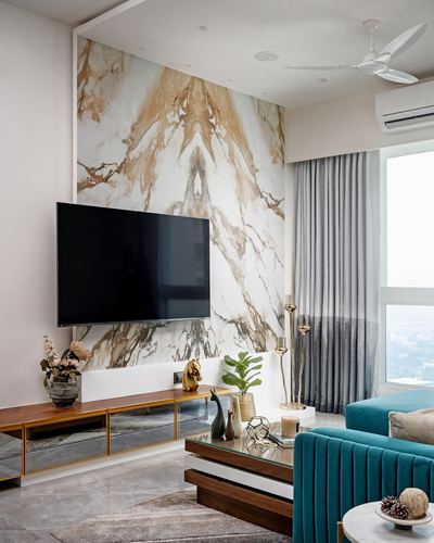 Living room with bookmatched gold-veined marble wall, mounted TV, wood console, and teal velvet sofa