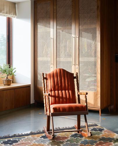 Orange velvet rocking chair before cane-paneled wooden wardrobes near a sunlit window