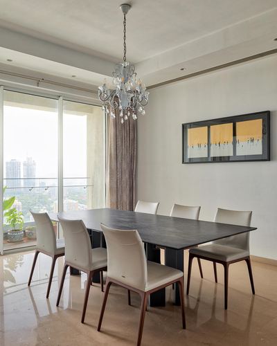 Minimalist dining room with dark stone table, chandelier, and city skyline view through glass doors
