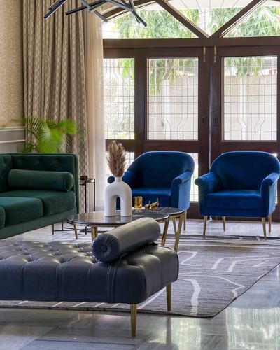 Living room with emerald sofa, blue velvet armchairs, and tufted bench facing lattice windows