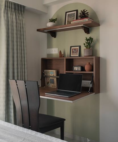 Wall-mounted fold-down wooden desk with laptop set into a sage-green arched niche