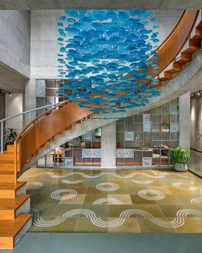 Spiral wooden staircase beneath a blue hanging art installation over patterned stone floor