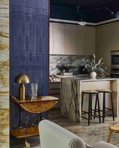 Kitchen with blue zellige tile wall, marble island, brass lamp on vintage bar cart