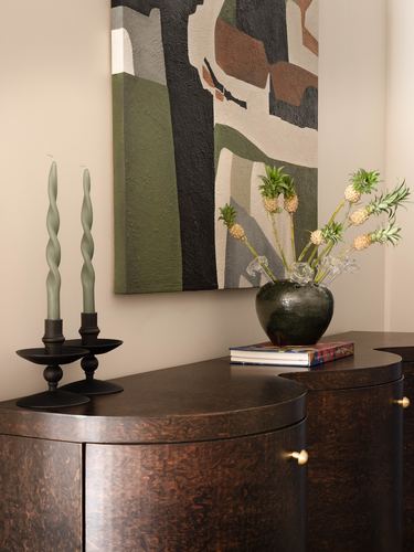 Curved burl-wood console with candles, ceramic vase, and abstract painting on wall