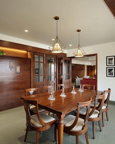 Wood-paneled dining room with carved chairs, long table, and two cage pendant lights over it