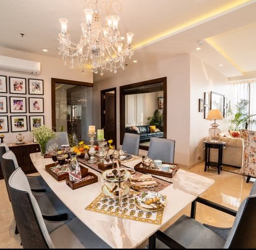 Dining room with marble table, crystal chandelier, gallery wall, and living area beyond