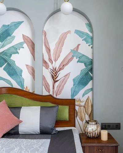 Bed with carved wood headboard beneath arched wall niches papered in botanical leaf mural.