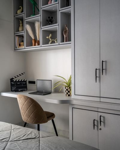 Grey built-in desk and cubby shelving with laptop, clapperboard prop, and tan velvet chair