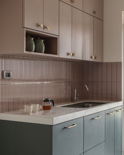 Pink fluted-tile kitchen backsplash with sage cabinetry, brass handles, and marble-look counter