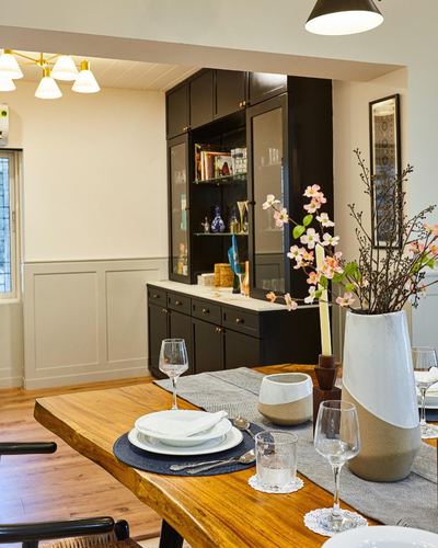 Live-edge wood dining table set with vases and branches in front of a black display cabinet