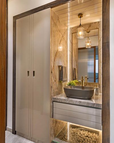 Bathroom vanity with dark oval sink, marble wall, brass pendants and wardrobe beside it
