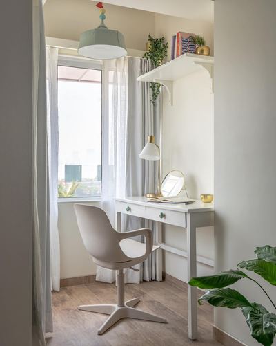 Small white study nook with desk, mirror, brass lamp, and pastel pendant by a window.